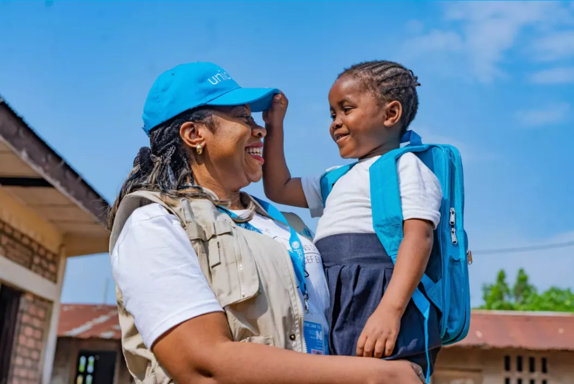 A smiling UNICEF volunteer holding a young child playfully in her arms.